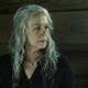 Carol, with long silver hair half-pulled into a tail, talks to someone in a wood-paneled room.